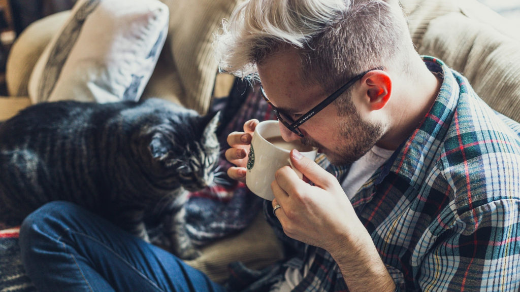 Man med kaffekopp och katt i soffan en kall höstdag